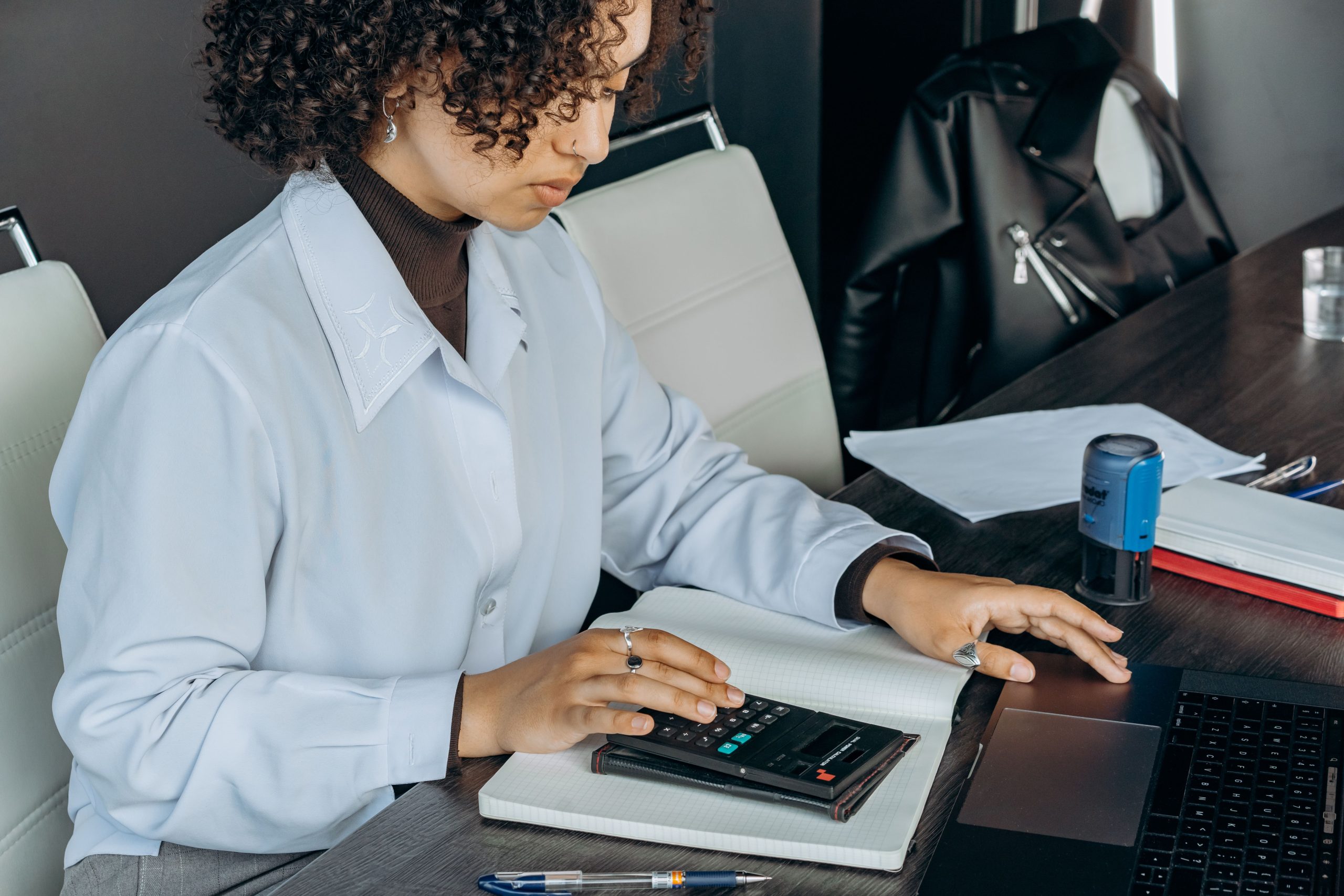 Bookkeeper using a calculator at a desk with a laptop and notebook